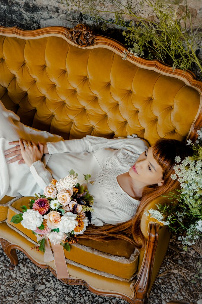Bride lounging on an orange sofa with orange and white bouquet