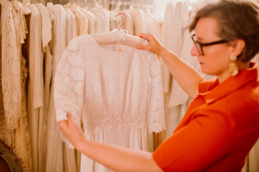Kate Ashwell holding a vintage lace wedding dress, in front of a rail of vintage bridal dresses