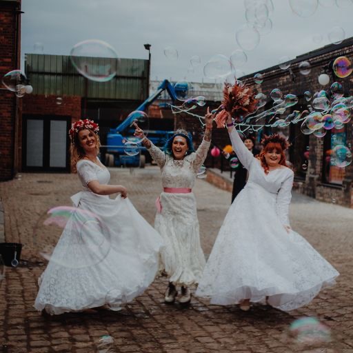 three women wearing wedding dresses dancing together and blowing bubbles